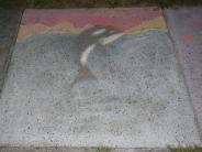 Sidewalk chalk art of black and white orca in blue water under red sunset