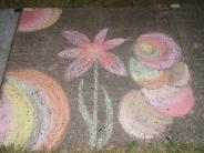 sidewalk chalk art pink flower with slender leaves and bright pink, green, blue and yellow baubles around them