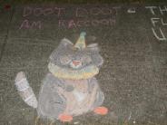 sidewalk chalk art includes black and white racoon very well drawn and colored with a blue and yellow collar and hat and clown